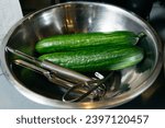 Small photo of Cucumbers in a metal bowl with a stainless steel peeler. Neatly arranged and accompanied by stainless steel peelers. Food preparation concept.