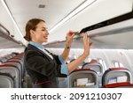 Cheerful flight attendant closing overhead luggage bin in airplane