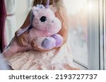 Little girl holding her soft toy unicorn while sit near window