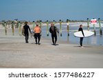 4 older surfers walking north at the poles in Hanna Park to surf some more