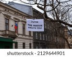 Small photo of Cracow, Poland - February 2022: A white banner with an inscription "Putin, The Hague awaits you!" hanging on a tree in front of the Russian Federation's General Consulate. Seleceted focus.