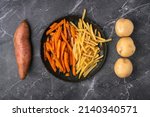 Symmetrical mix of sweet potato fries, French fries and raw vegetables on a dark background, top view
