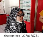 Small photo of Yogyakarta, Indonesia October 18, 2023. Young women wear trial frame glasses, an eye health examination tool. minus eye care at an optical shop, replacement of minus glasses.