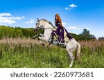 Small photo of Purple-clad medieval princess galloping behind a growing white horse. Background: Field grasses with a spruce forest, spring, and summer in the distance the horse rears up.