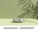 Small photo of An empty podium made of gray stone on a green background with a shadow of tropical leaves. Scene for the promotion of products, beauty, natural eco-cosmetics. Showcase, display case.