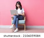 Asian woman sitting on sofa using laptop with happy expression	