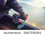 Small photo of Solar panel technician with drill installing solar panels on roof. technician in blue suit installing photovoltaic blue solar modules with screw. Electrician panel sun sustainable resources
