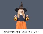 A happy laughing little girl in a witch costume and makeup holds pumpkin baskets for Halloween treats on a dark background. Children's Halloween