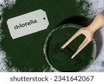 Small photo of Blue-green algae Chlorella and spirulina powder in bowl with paper note text CHLORELLA. Super powder. Natural supplement of algae. Detox superfood drink cocktail. Food supplement source of protein and