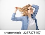 Small photo of Side view of young smiling beauteous woman with closed eyes raising hands, holding short fair wavy hair, touching head, wearing glasses, denim shirt, white T-shirt on white background. Copy space.
