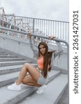 Small photo of Slender smiling fitness girl with perfect legs looks into camera sitting on stadium stairs. Fitness classes. Health and figure correction. Positive emotions. Charge of vivacity and energy.