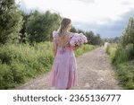 Image from back of unrecognizable woman with bouquet of pale pink peonies on summer day on country road . Femininity and beauty. Positive emotions. Serene mood. Business of growing flowers. 