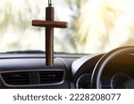 Closeup wooden crucifix hang  in  front steering wheel and console of the car. Concept, talisman,amulet to prevent accidents. Belief, faith,holy  in god to protect when driving.                       