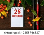 Small photo of calendar date on wooden dark desktop background with autumn leaves and small apples. September 28 is the twenty-eighth day of the month.
