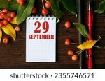 Small photo of calendar date on wooden dark desktop background with autumn leaves and small apples. September 29 is the twenty-ninth day of the month.