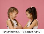 Small photo of two angry little girls in dress looking at each other on pink background. children's grievances and quarrels