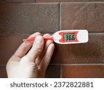 Small photo of hand with an electronic thermometer on the background of a brick wall. epidemics, virus and morbidity season. fever during illness