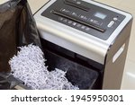 Document shredder with paper shreds on garbage black bag and tray garbage.