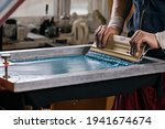 selective focus photo of male hands with squeegee. serigraphy production. printing images on t-shirts by silkscreen method in a design studio