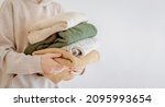 Small photo of Woman's hand holding a stack of clothes. Clothes Donation, Renewable Concept.Preparing Garment at Home before Donate. Woman packs clothes for a donation or for moving