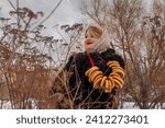 Small photo of Russian woman in fur coat and folk down shawl with bagels. Shrovetide, Lent. slavic core, Russian culture.