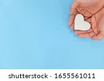Hands holding a white heart in blue background with copy space. Kindness, charity, pure love and compassion concept.