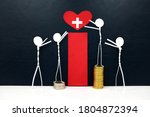 Small photo of Stick figure reaching for a red heart shape with cross cutout while stepping on stack of coins. Health care and hospital access inequity and disparity concept.