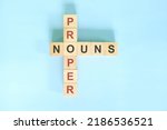 Small photo of Proper nouns concept in English grammar education. Wooden block crossword puzzle flat lay in blue background.