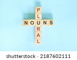 Small photo of Plural nouns concept in English grammar education. Wooden block crossword puzzle flat lay in blue background.