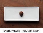 Small photo of Photo of an isolated roasted chesnut on a with elongated dish on a wooden table