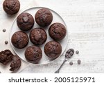 Chocolate muffins on white ceramic plate. Homemade fluffy and moist chocolate cakes. Top view. Copy space. White wooden table background.
