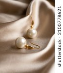 Small photo of Pearl earrings with golden fittings on shiny beige silk background. Beautiful accessories for women. Elegant jewelery gift or present for wedding or saint valentine's day.