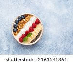 Small photo of Muesli and yogurt bowl decorated with fresh blueberry, raspberry, banana slices, chia seeds, coconut shred and mint leaf. Healthy vegetarian breakfast or snack. Top view. Copy space. Blue background.