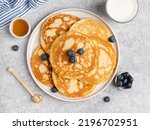 Pancakes stacked on white ceramic plate with honey and blueberry. Tasty breakfast, lunch or snack. Top view, close up food, kitchen napkin. Grey background. Morning table.