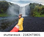 Asian woman in yellow jacket holding hands with couple at front of Skógafoss waterfall flowing on cliff in summer at South of Iceland