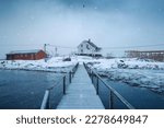 Nordic white house on coastline and wooden bridge in blizzard among fishing village at Lofoten Islands, Norway