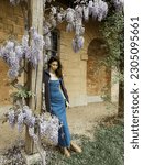 Small photo of a woman in denim dress and embroidered jacket by blooming flowers near Marie Antoinette's little house