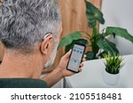 Small photo of Hearing impaired mature man adjusts settings for his BTE hearing aid via smartphone. Hearing aids, deafness treatment, innovative technologies at audiology