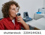 Small photo of Curly boy performing pulmonary function test and spirometry using spirometer at medical clinic. Spirometry of child's lungs