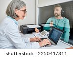 Small photo of Experienced female audiologist doing hearing test to male patient in soundproof audiometric booth with audiometer in hearing clinic. Audiometric testing