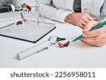 Small photo of Audioprosthetist presentation hearing aids in two colors to his patient lying on table near otoscope and display stand with BTE hearing aids