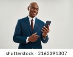 Smiling black businessman watching mobile phone. Bald adult man wearing formal wear. Concept of modern successful male lifestyle. Isolated on white background. Studio shoot. Copy space