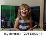 Small photo of angry little girl deliberately smashed the TV with a hammer and is happy. uncontrollable child with conduct disorders