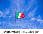 Small photo of Italian flag waving in the wind on the balcony. Patriotic. National Italian flash mob. Coronavirus. Epidemic. Flag of country and the blue sky. Copy paste. Blurred background. Selective focus.