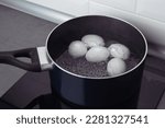 A pan with some boiling eggs on a stove. White eggs in boiling water. Cooking process.