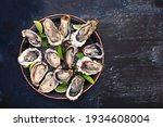 Fresh oysters with lime on a round plate. Oyster season. Seafood dish on a blue background. Oyster on the half shell. Top view.Free space.