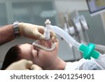 Small photo of A child with an oxygen mask on his face. Preparing child for anesthesia. Dental surgery under general anesthesia. Surgical intervention. Dental treatment under general anesthesia. Side view.
