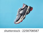 Stylish trendy sports shoes hanging on blue background. Men's fashion sport footwear. Air sneakers. Levitation concept. Flying colored leather sneakers isolated on a pastel background.
