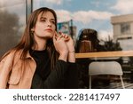 Close up caucasian young pretty stylish woman sitting table near street cafe restaurant chill dressed brown trench coat smiling happy poses outside in city, spring autumn season. Cute brunette hair la