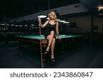 Blond woman playing enjoying billiard, hold cue, white billiard balls on table with green surface in billiard club. Pool game snooker pyramid player

